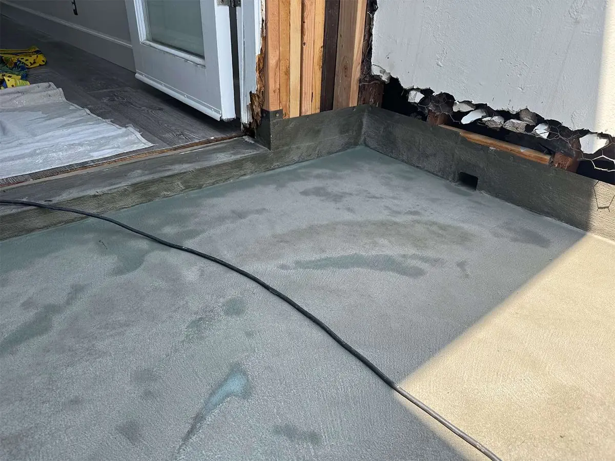 Concrete floor drying inside a partially exposed building wall. An open door and visible cable suggest ongoing renovation work.
